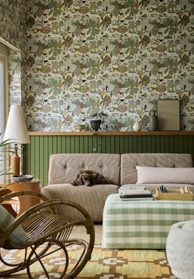 Living space featuring green wildlife print wallpaper (Animal Kingdom - Pea) with green panelling behind a sofa, foot stool and a rocking chair.