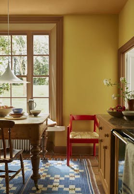 Kitchen painted in rich yellow shade 'Yellow-Pink' with deep gold 'Affogato' on the window frame, mid gold 'Middle Buff' on the ceiling and a bright red chair.