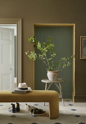 Hallway painted in earthy green shade 'Light Bronze Green' with the alcove in muted green 'Ambleside' next to a gold velvet bench.