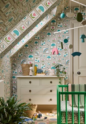 Nursery featuring neutral photo frame print wallpaper (Balance - Portland Stone) with a dresser, green crib and a plant.